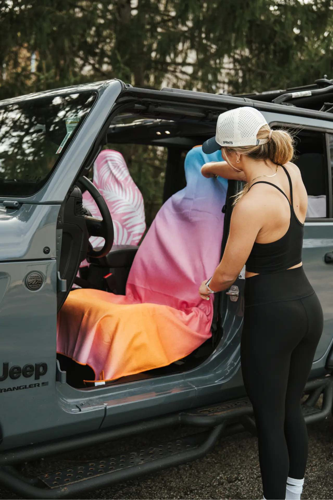 Woman draping a Sprints car seat cover towel over the driver seat of a Jeep Wrangler